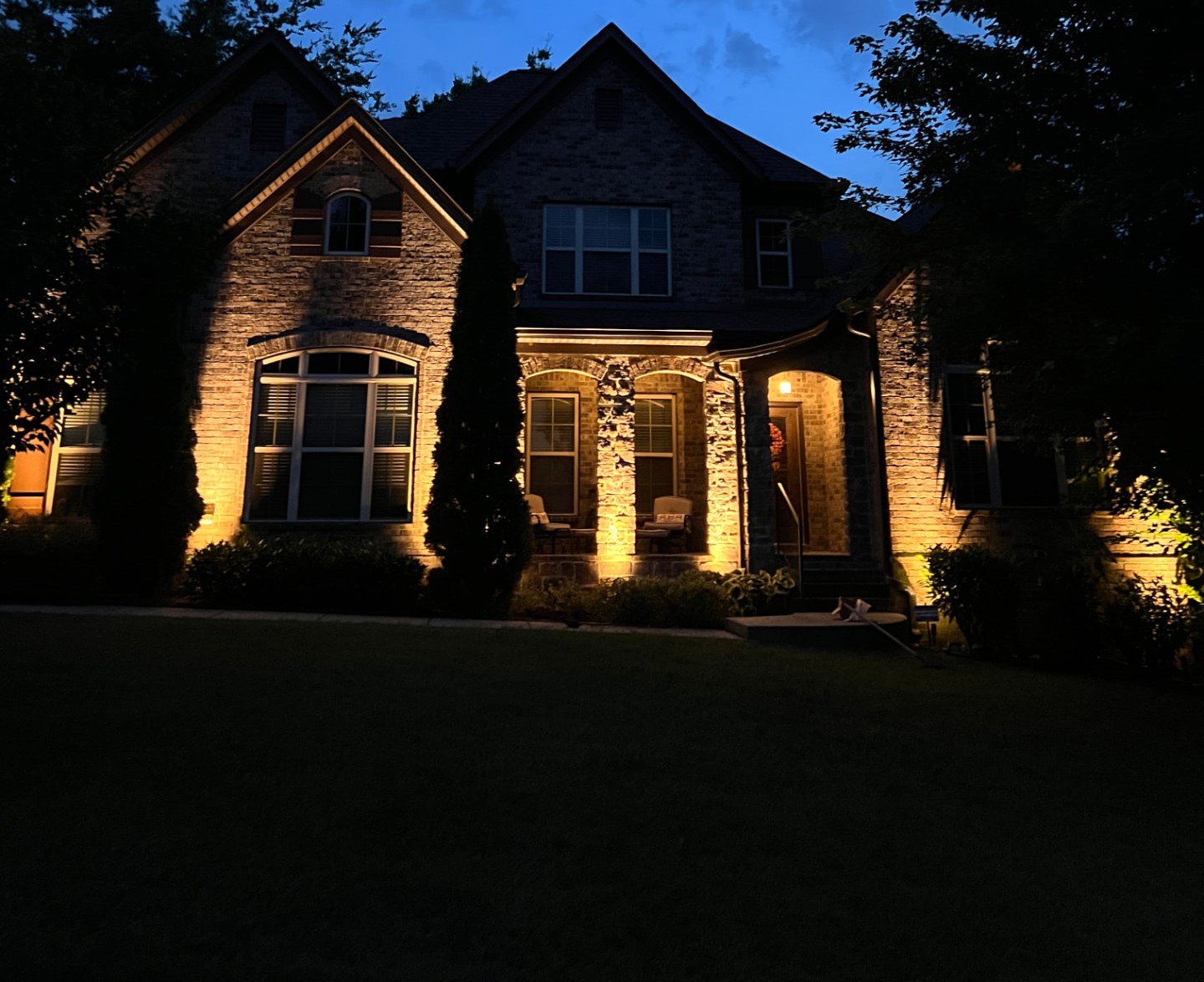 Luxury brick home at night with golden landscape lighting and manicured lawn