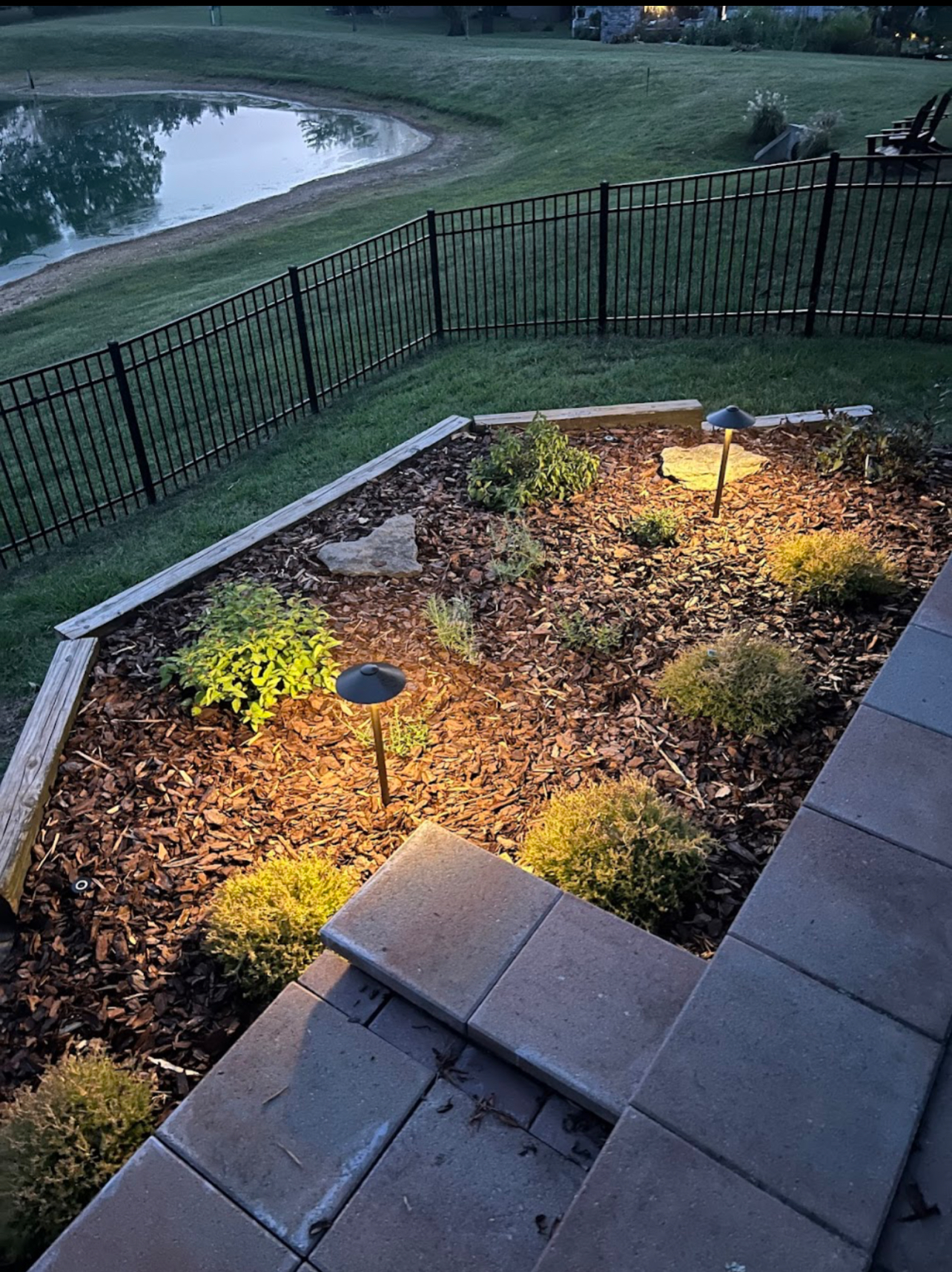 Landscape lighting illuminating a mulched garden bed at dusk