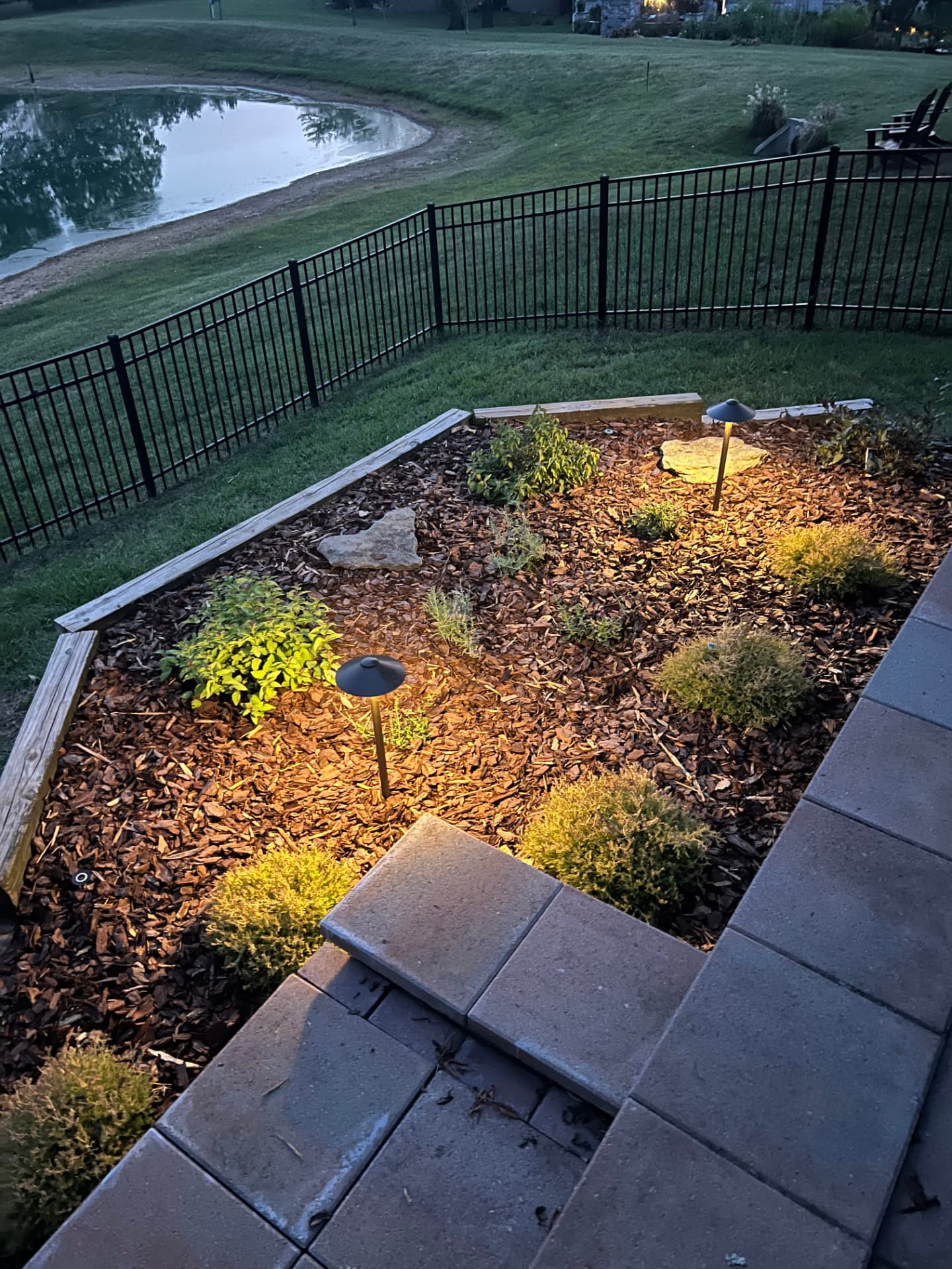 Paver patio overlooking a landscaped garden bed with accent lighting and a lake view